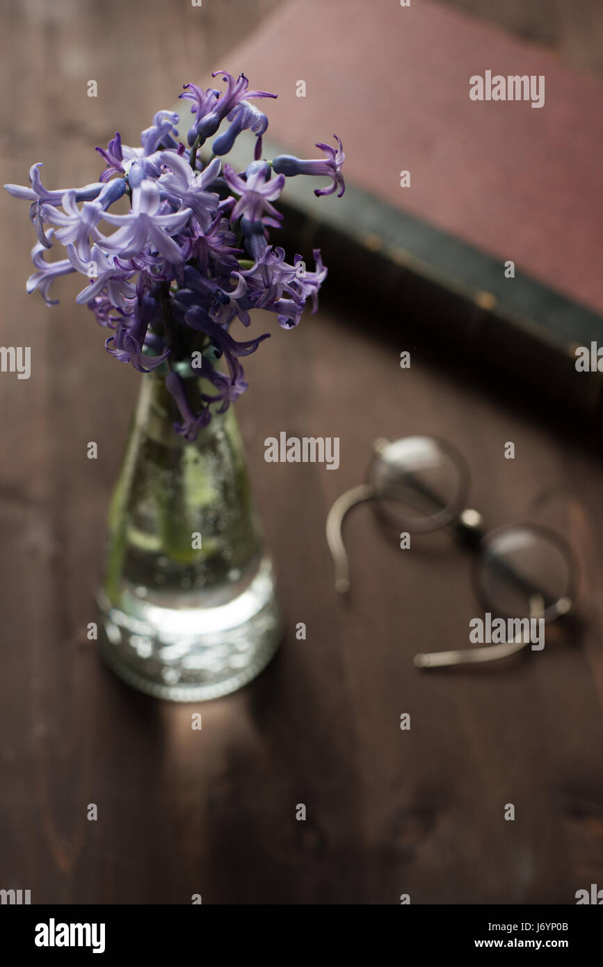 Hyacinths in a vase, spectacles and an old book on a wooden table Stock Photo