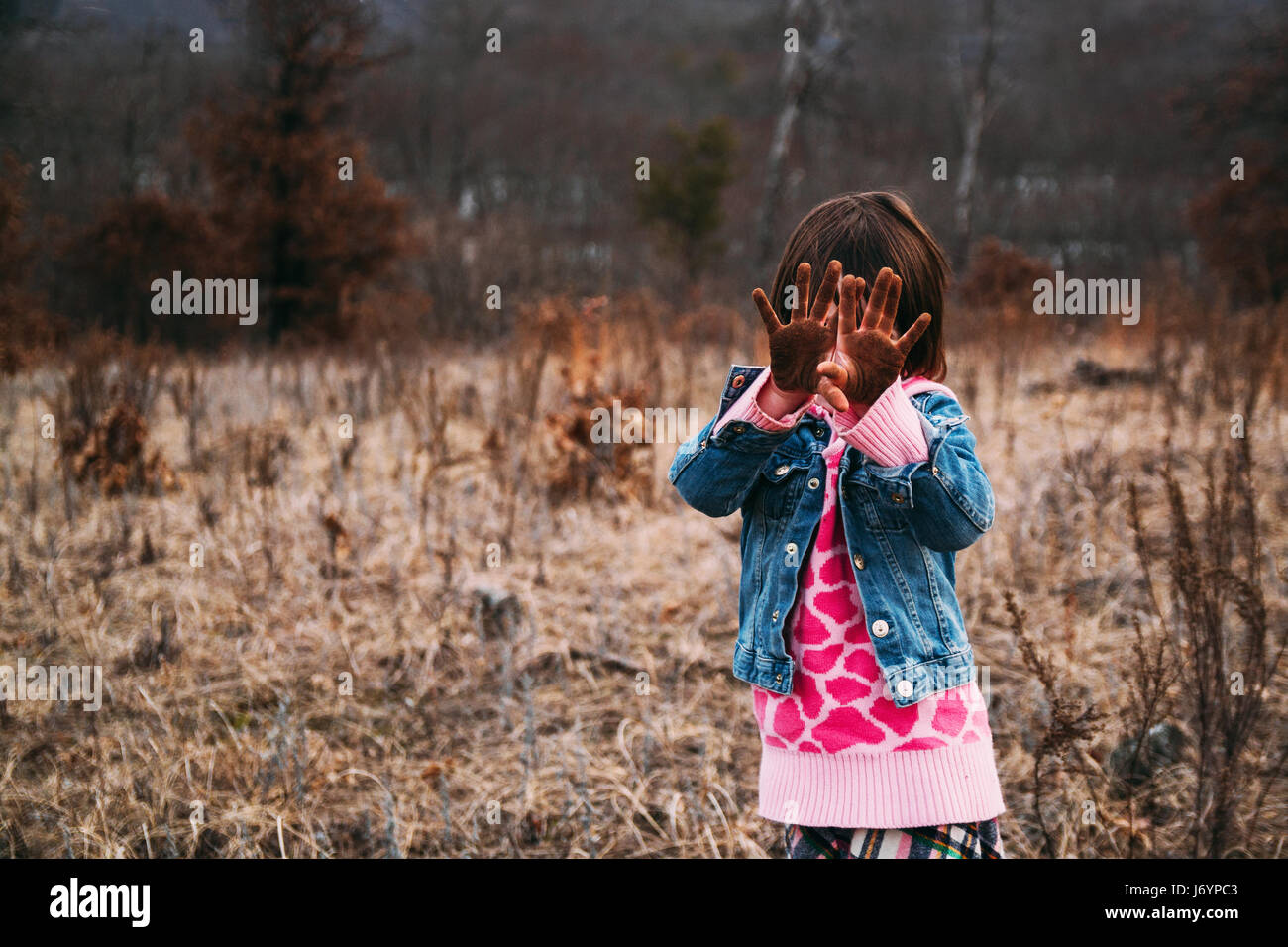 Girl standing in rural landscape holding dirty hands in front of her face Stock Photo