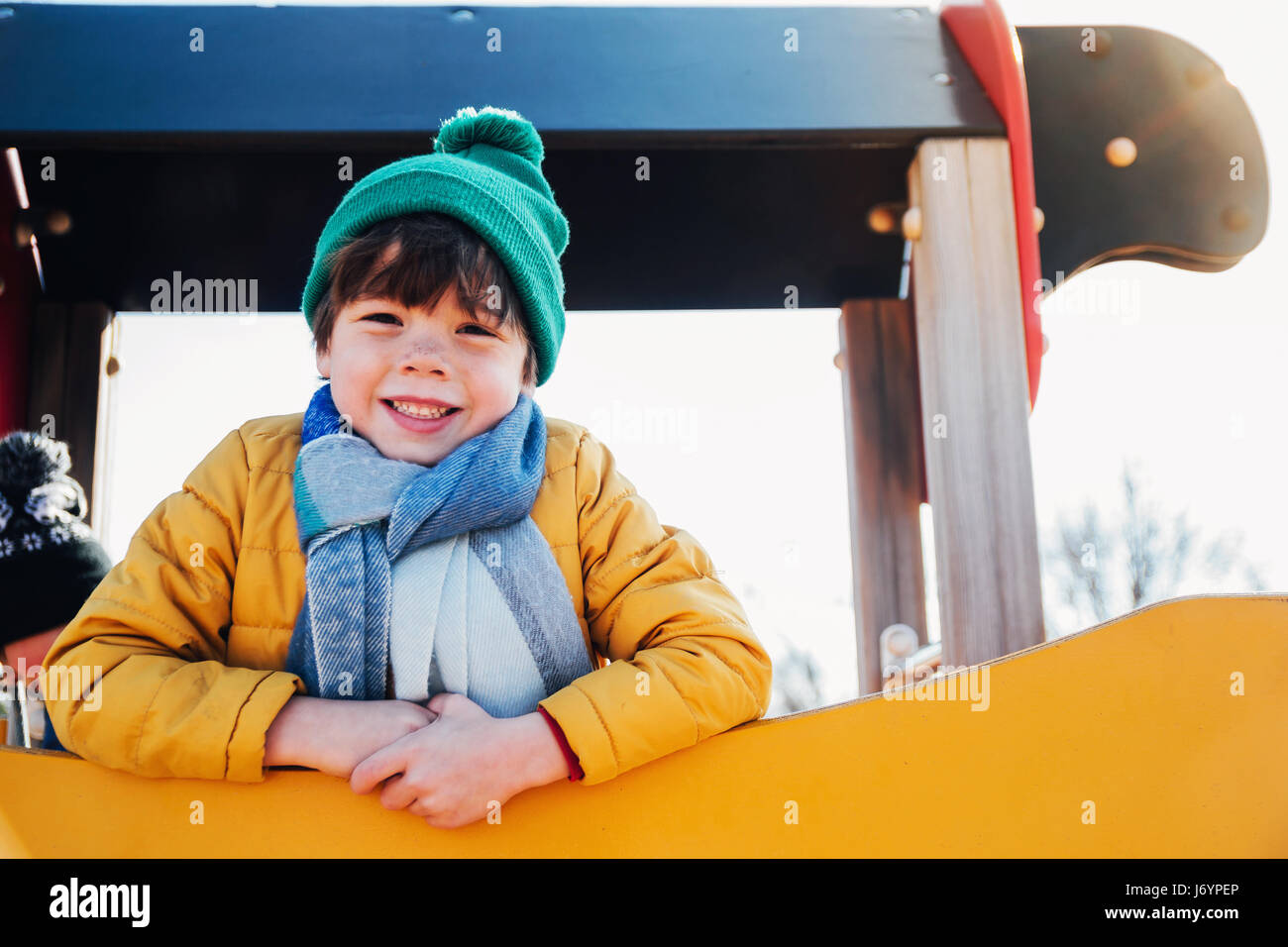 Boy in warm clothing standing on climbing frame in playground Stock Photo