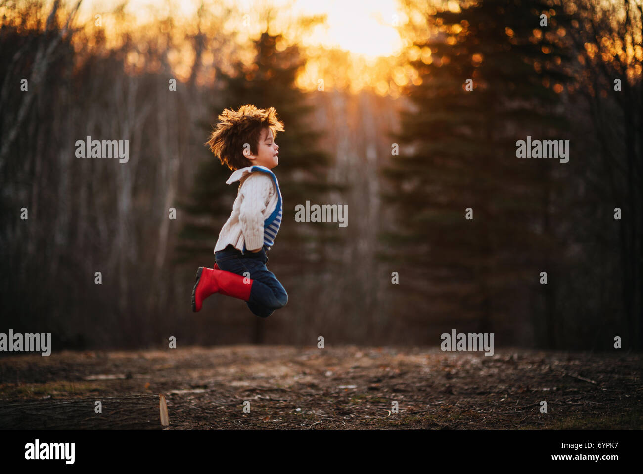 Boy jumping off a log in the forest Stock Photo