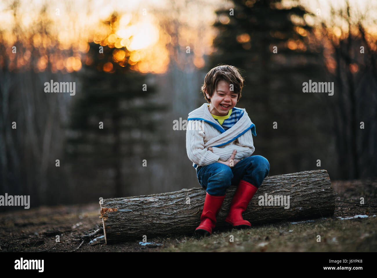 Boy sitting on a log laughing Stock Photo