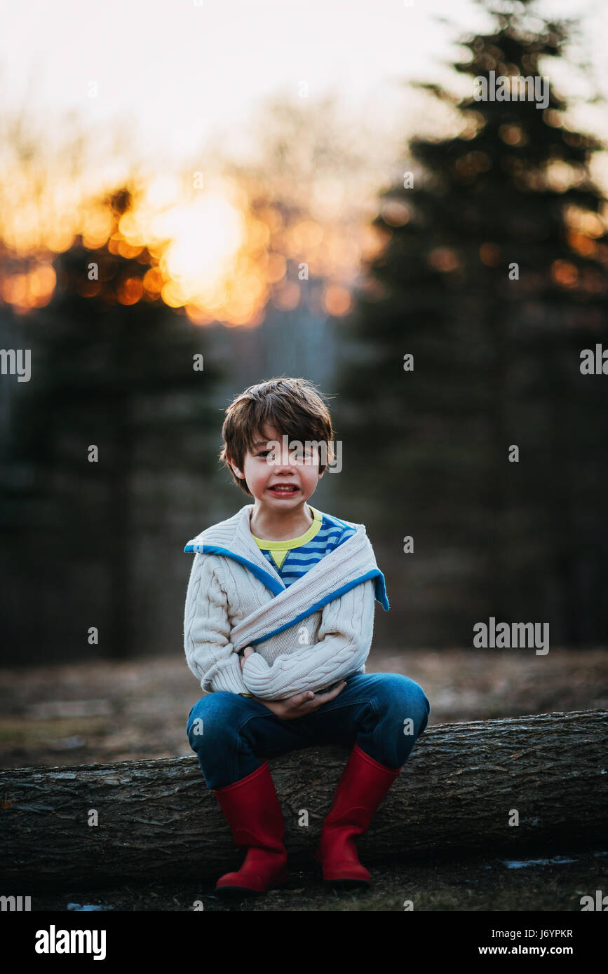 Boy sitting on a log laughing Stock Photo
