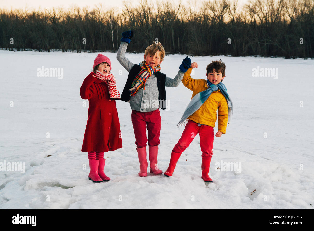 Three children standing in the snow with arms raised shouting Stock Photo