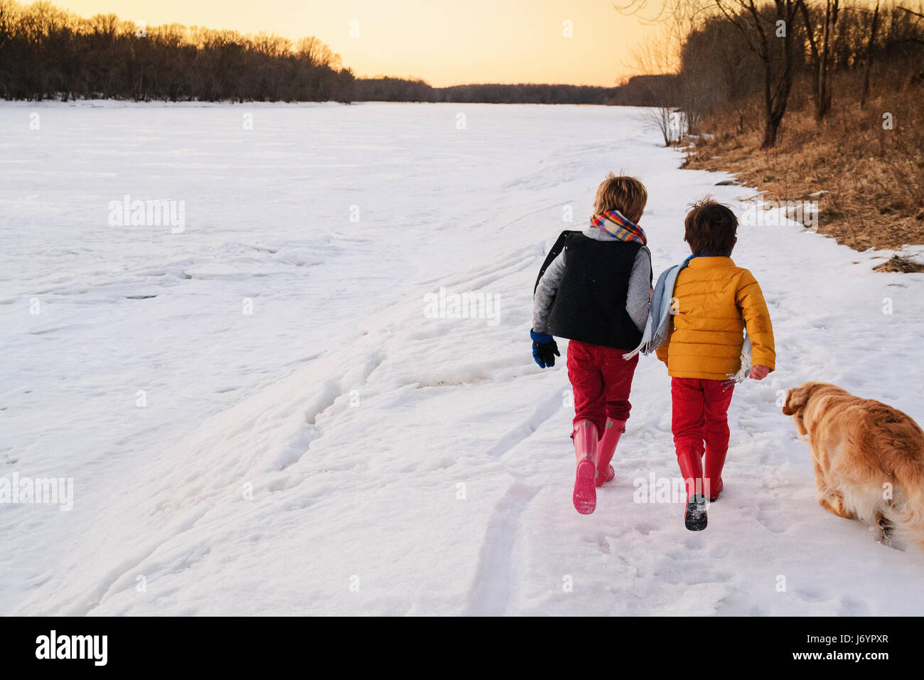 Two boys and a dog running on a frozen river in the evening Stock Photo