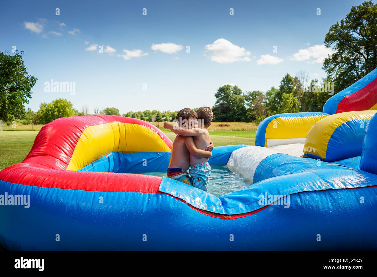 Two boys hugging on an inflatable water slide Stock Photo