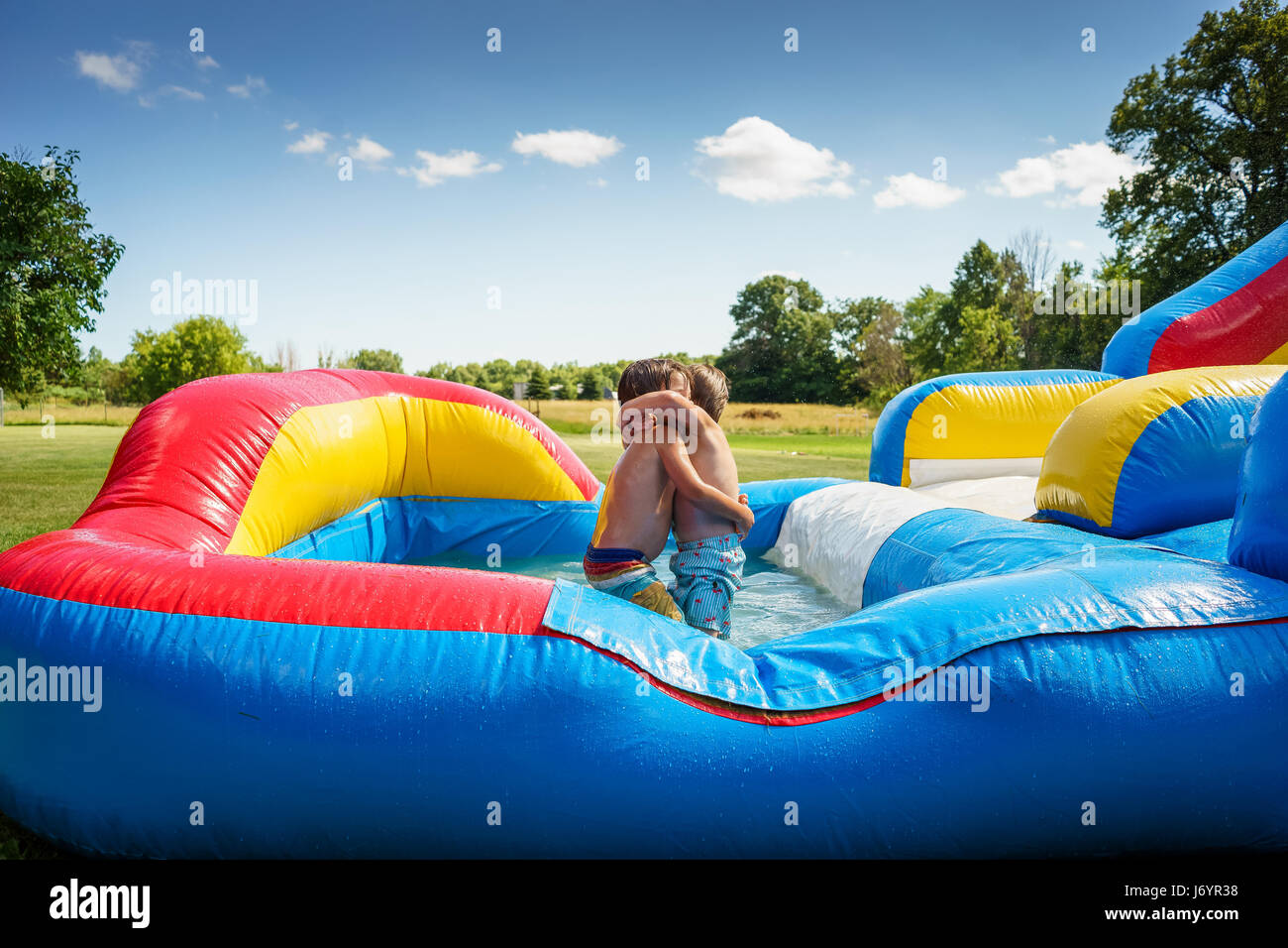 Two boys hugging on an inflatable water slide Stock Photo