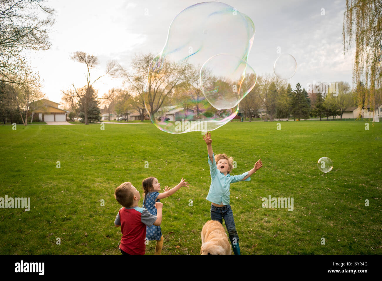 Three children playing with giant soap bubbles Stock Photo