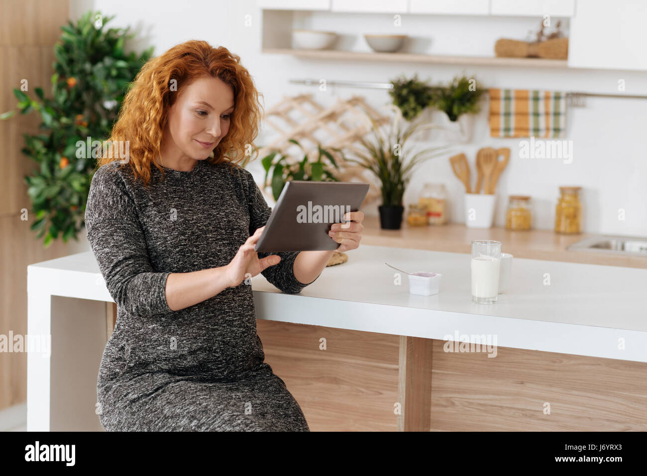 Curly-haired expectant woman working on digital tablet Stock Photo
