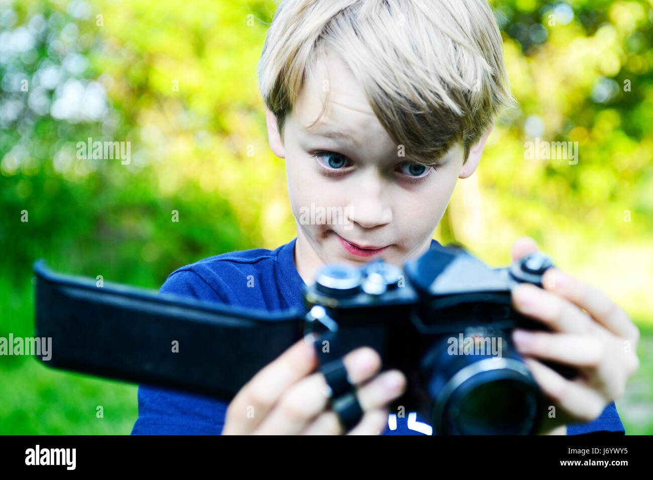 Sad boy looking at the open back of the camera and enlightened ruined film inside. Little child blond boy with an old camera shooting outdoor. Kid tak Stock Photo