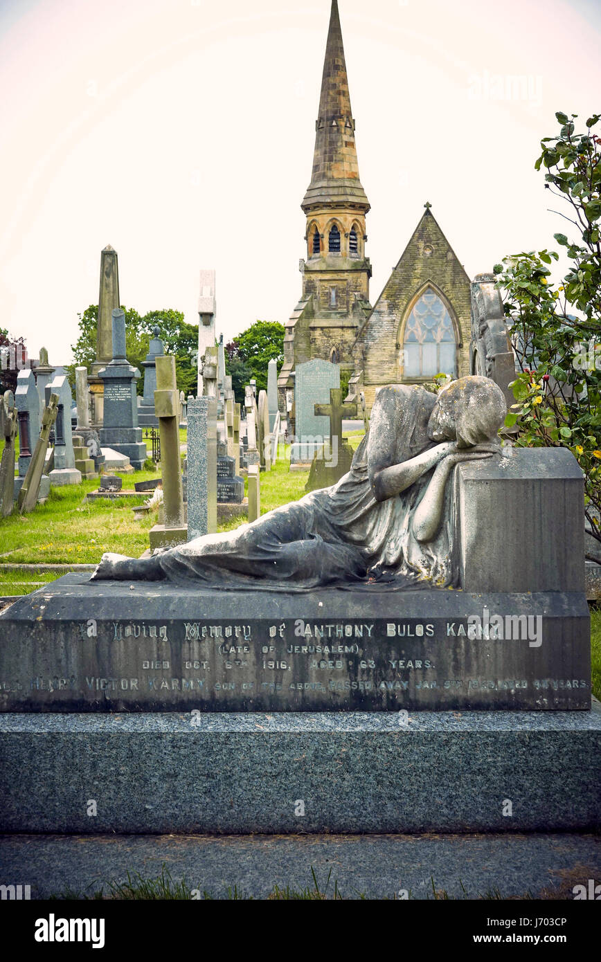 Statue of prone sleeping figure on grave with chapel steeple behind Stock Photo