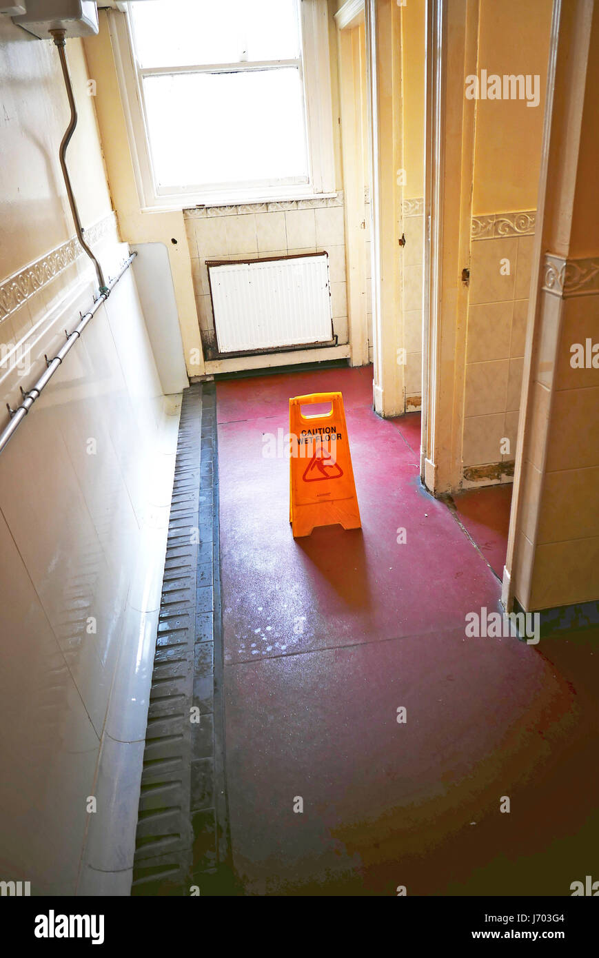 Yellow plastic caution wet floor sign in gents toilets to warn users of a slip hazard Stock Photo