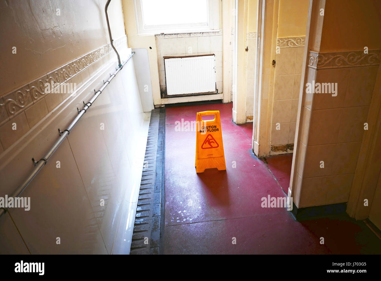 Yellow plastic caution wet floor sign in gents toilets to warn users of a slip hazard Stock Photo