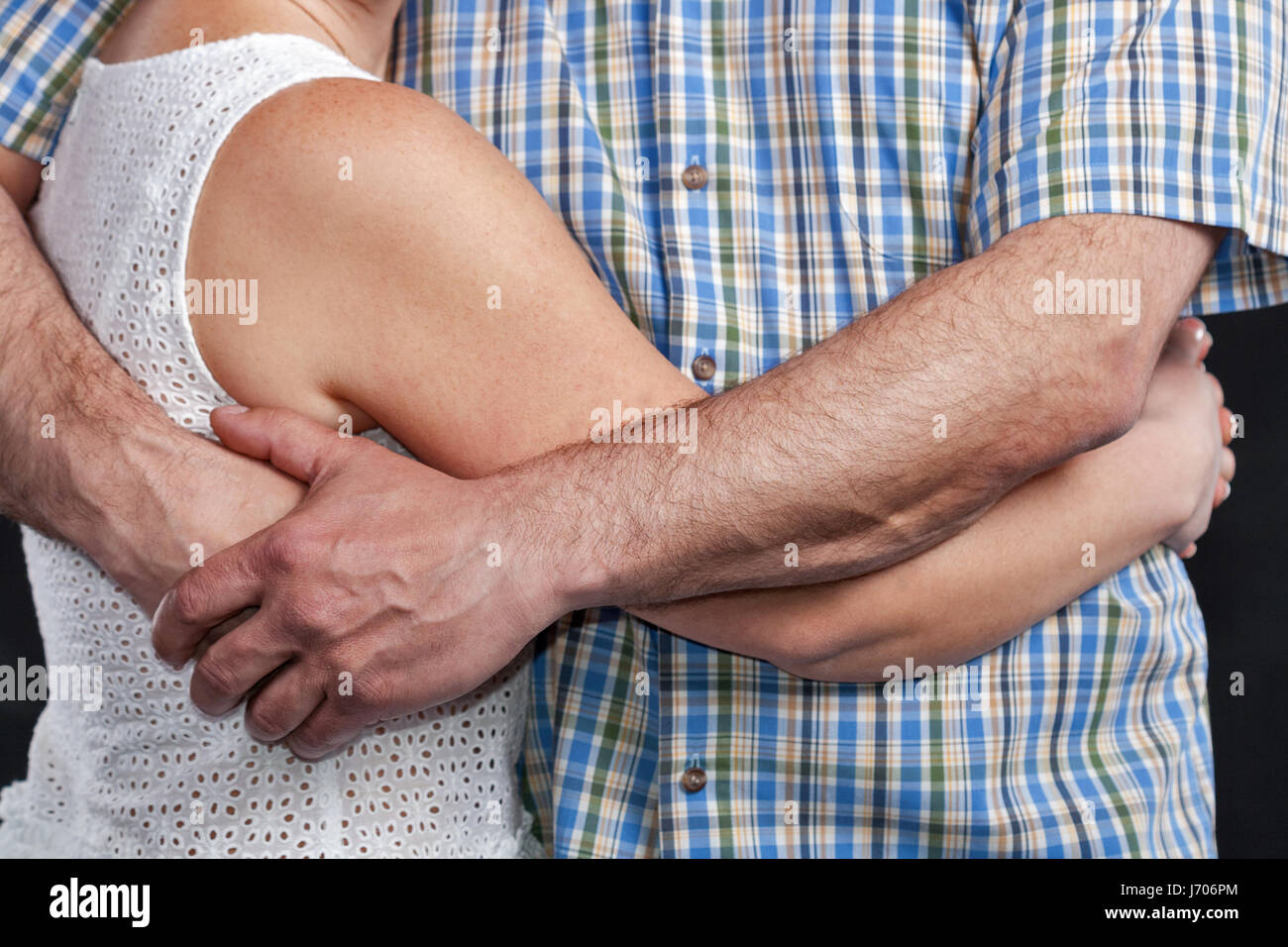 Unrecognized caucasian middle aged woman in white dress and man in plaid shirt embrace one another, closeup Stock Photo