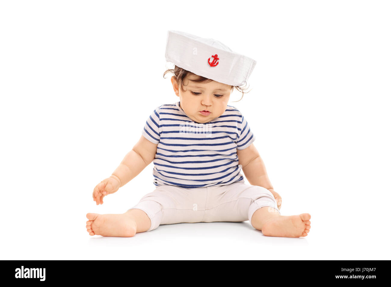 Baby girl dressed in a sailor outfit sitting on the floor isolated on white background Stock Photo