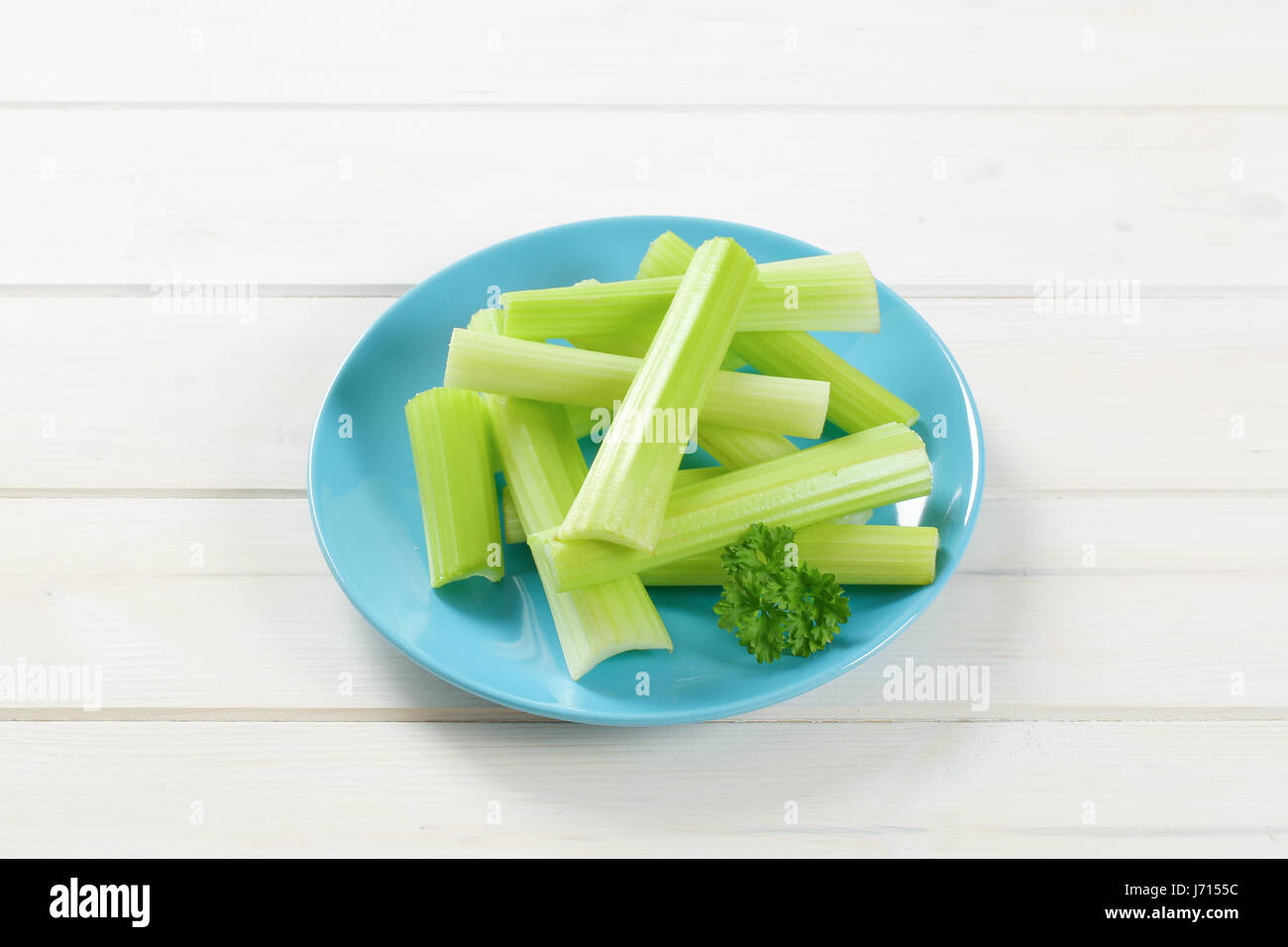 plate of green celery stems on white wooden background Stock Photo