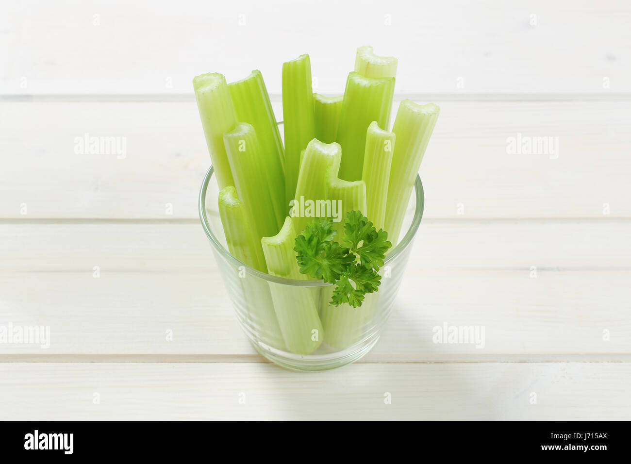 glass of green celery stems on white wooden background Stock Photo