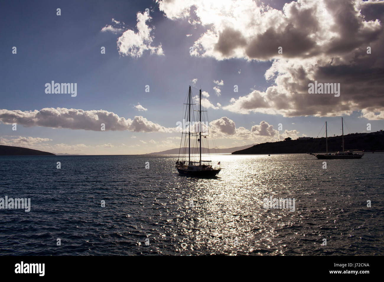 Sun light breaks through clouds in dramatic sky. It shines on sea surface in Bodrum southwestern Turkey. Reverse light make yachts and landscape look  Stock Photo