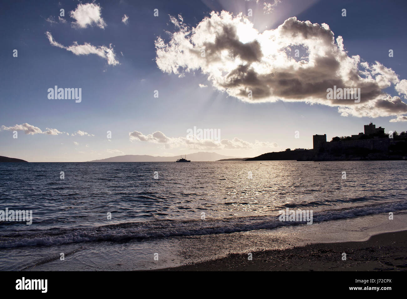 Sun light breaks through clouds in dramatic sky. It shines on sea surface in Bodrum southwestern Turkey. Reverse light make Bodrum castle look as silh Stock Photo
