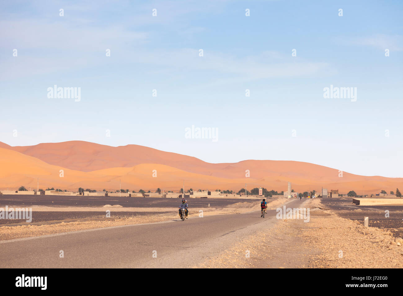 Motorbike and bicyclist driving on a desert road near Merzouga, Morocco Stock Photo