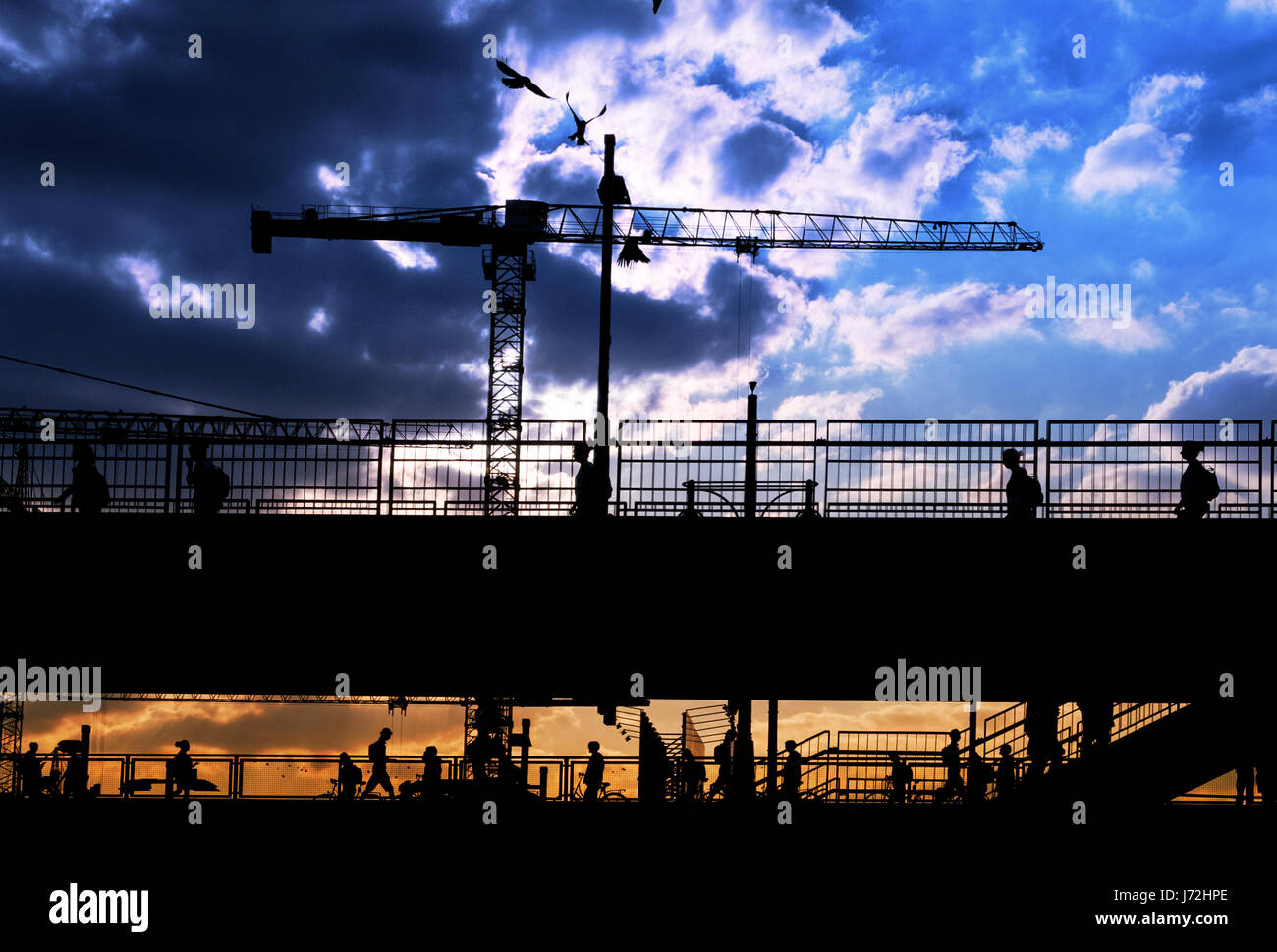 silhouettes of many people crossing bridge with sunset sky background Stock Photo