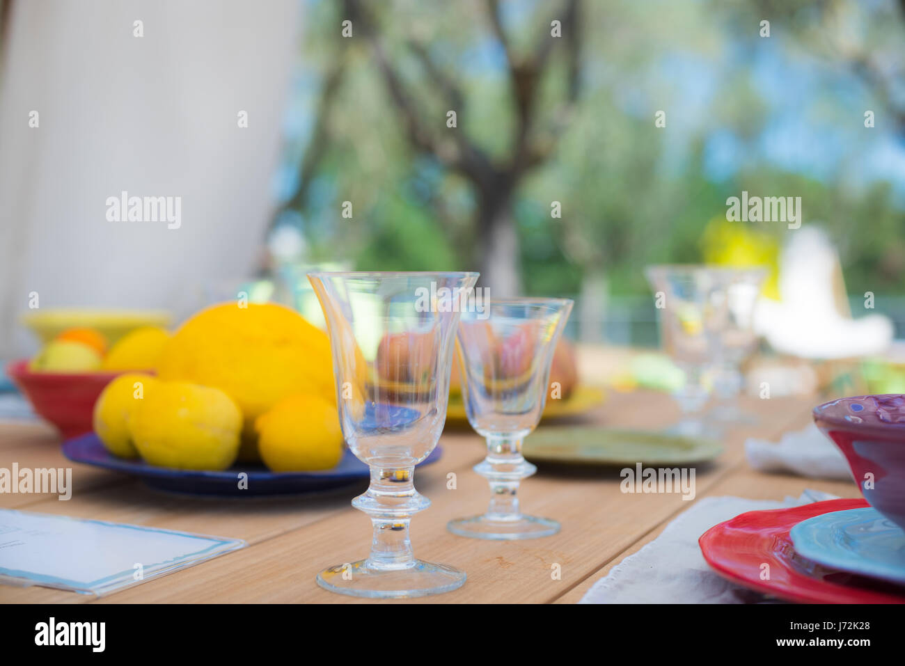 Dining set on outdoor table, focus on glasses, relax and tranquil feeling with lemon fruits in plate in background Stock Photo