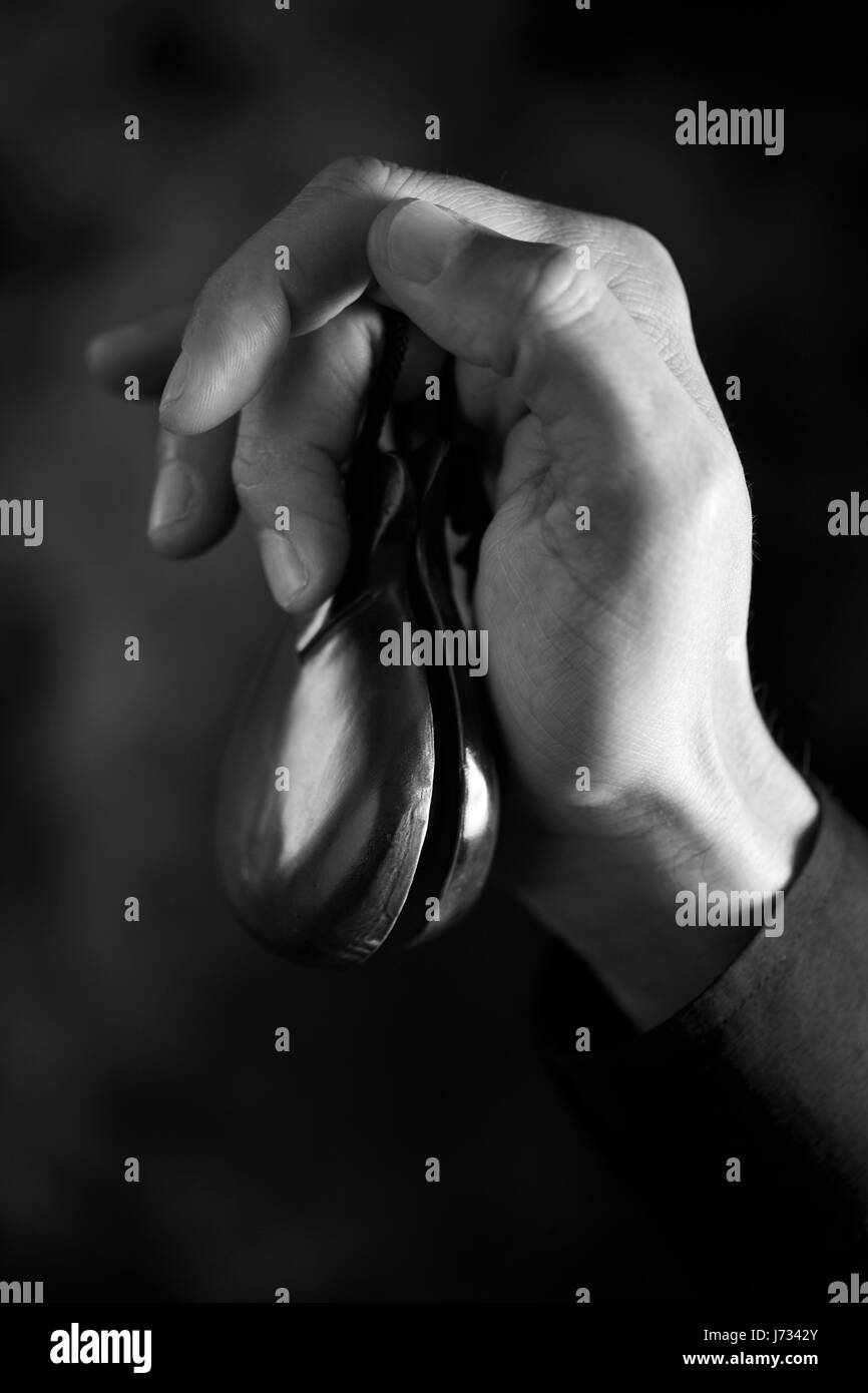 closeup of the hand of a young caucasian man playing the castanets against a dark background, in black and white Stock Photo