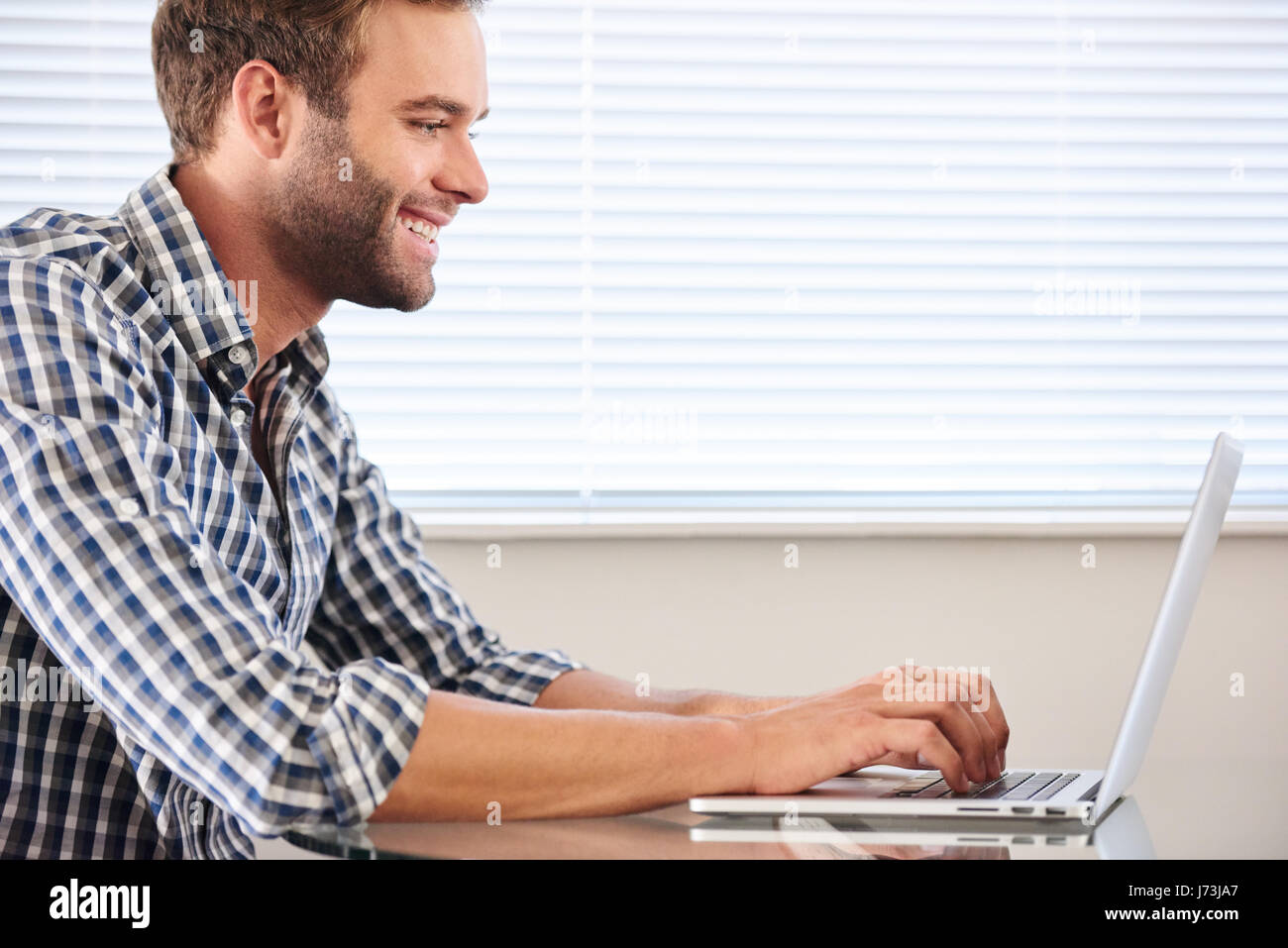 profile image of handsome groomed man typing on laptop computer Stock Photo