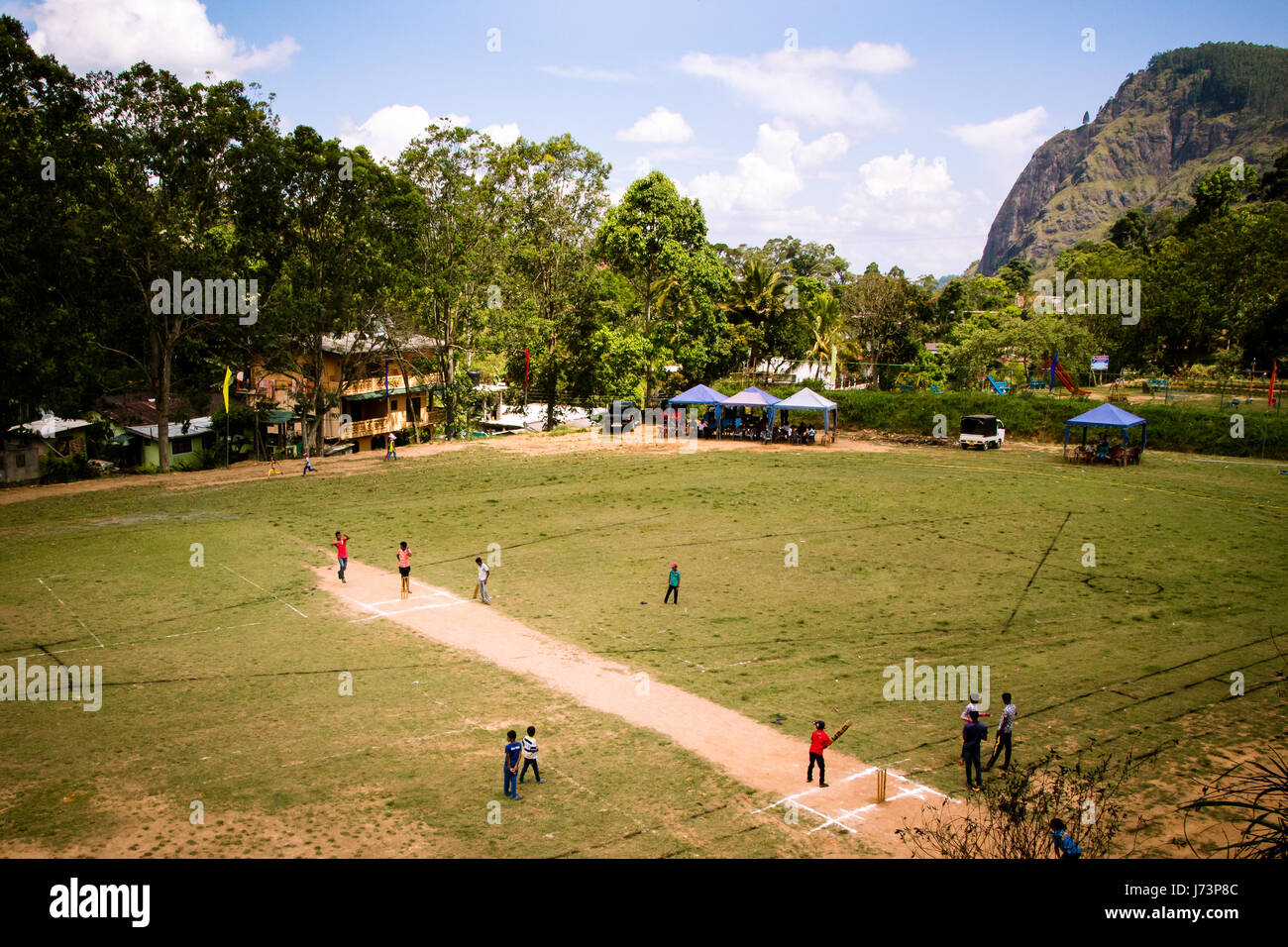 Children play cricket at the local grounds in Ella, Sri Lanka. The mountain known as Ella Rock can be seen in the background. Stock Photo