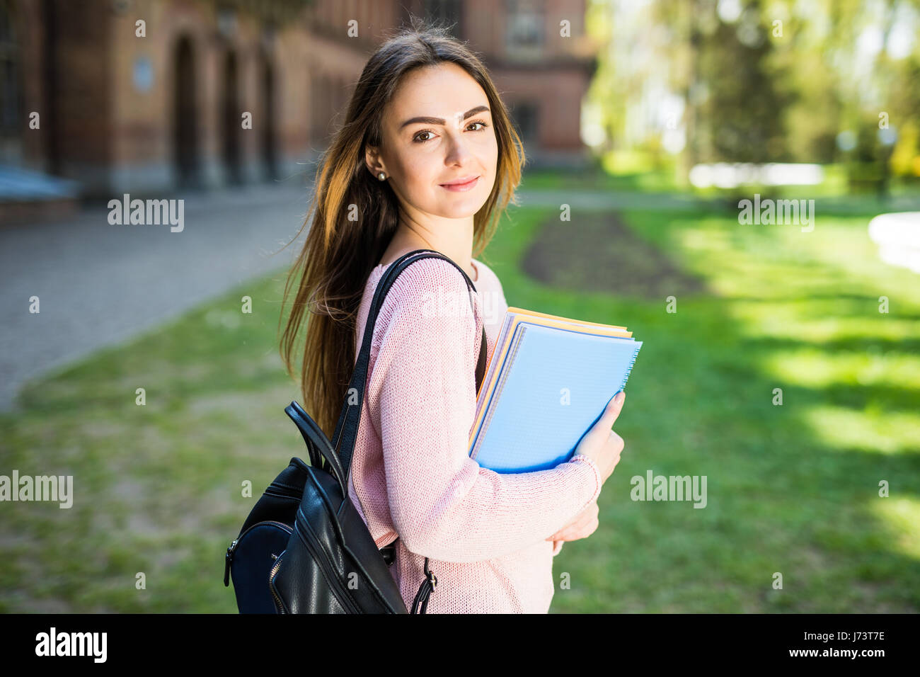 University student girl looking happy smiling with book or notebook in campus park. Caucasian young woman female model. Stock Photo