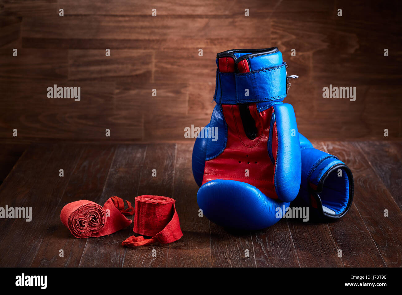 Pair of red and blue boxing gloves and red bandage on brown plank Stock