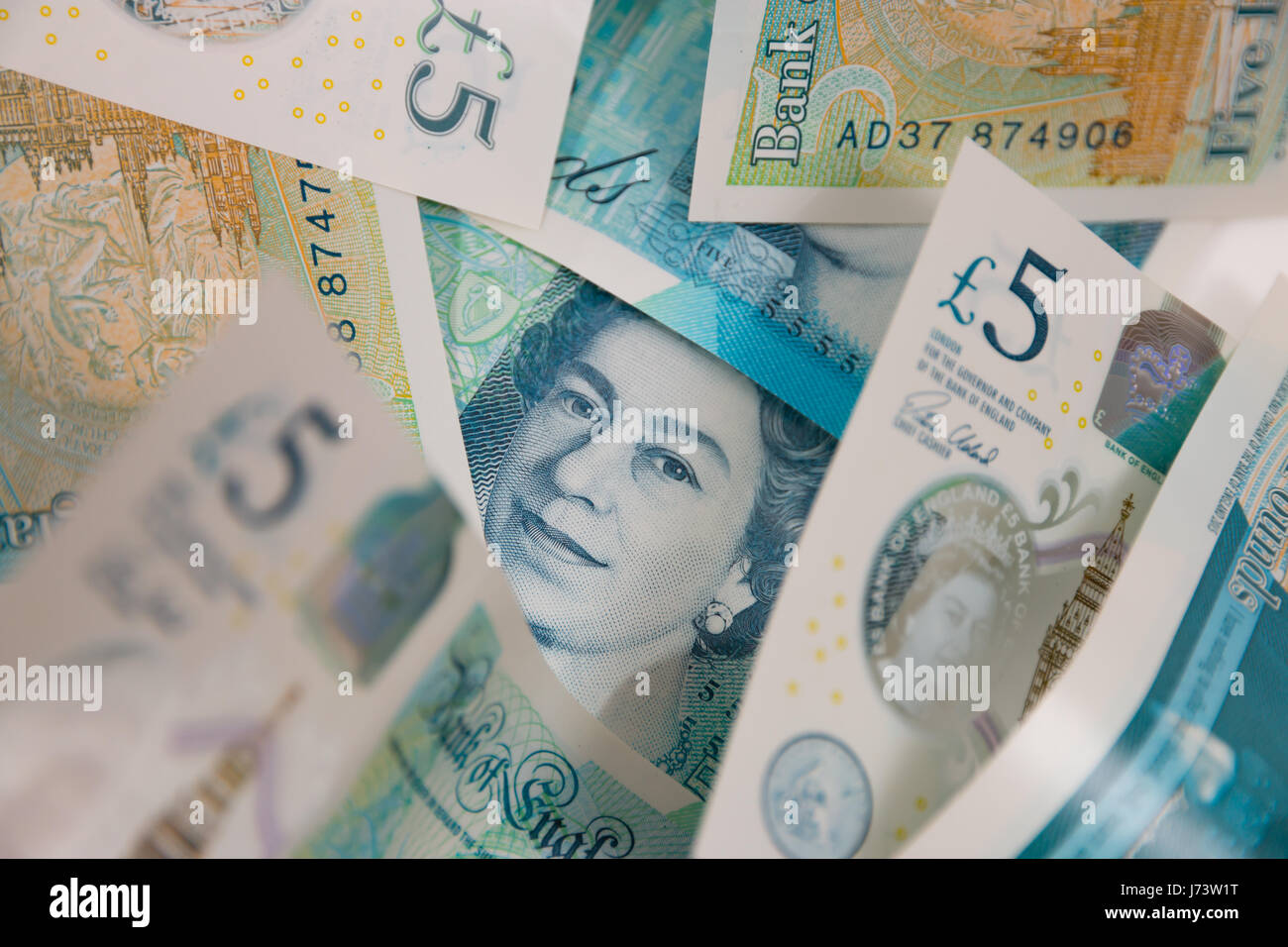 The face of Queen Elizabeth II staring out from a pile of five pound notes Stock Photo