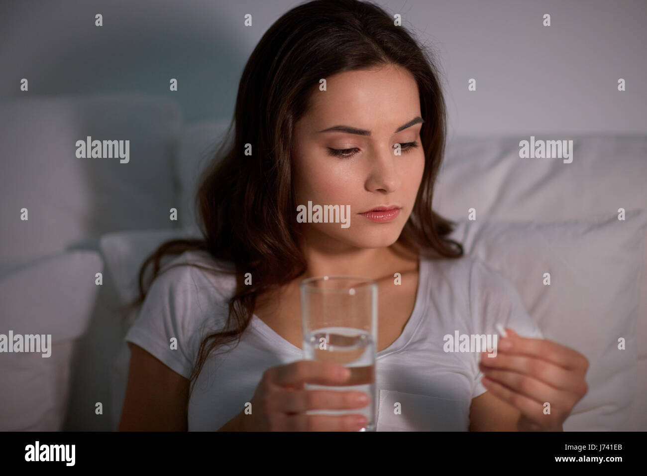 woman with pill and glass of water in bed at home Stock Photo