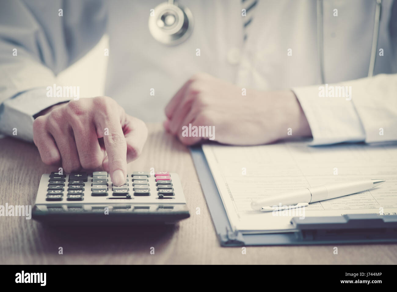 closeup of a young caucasian healthcare professional wearing a white coat calculates on an electronic calculator Stock Photo