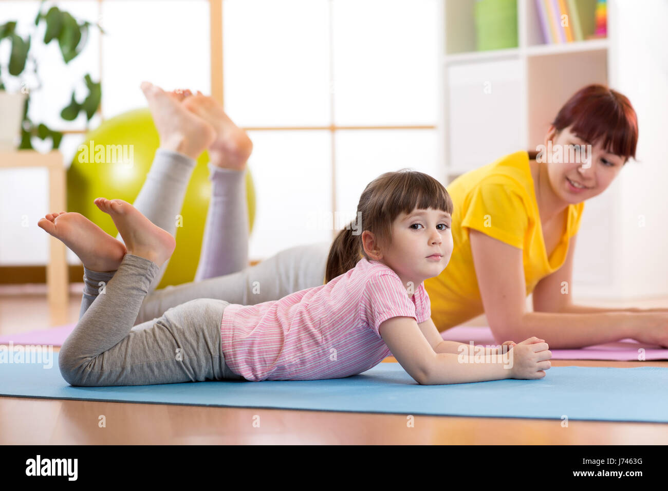 Mother and daughter doing gymnastics exercises on mat at home Stock