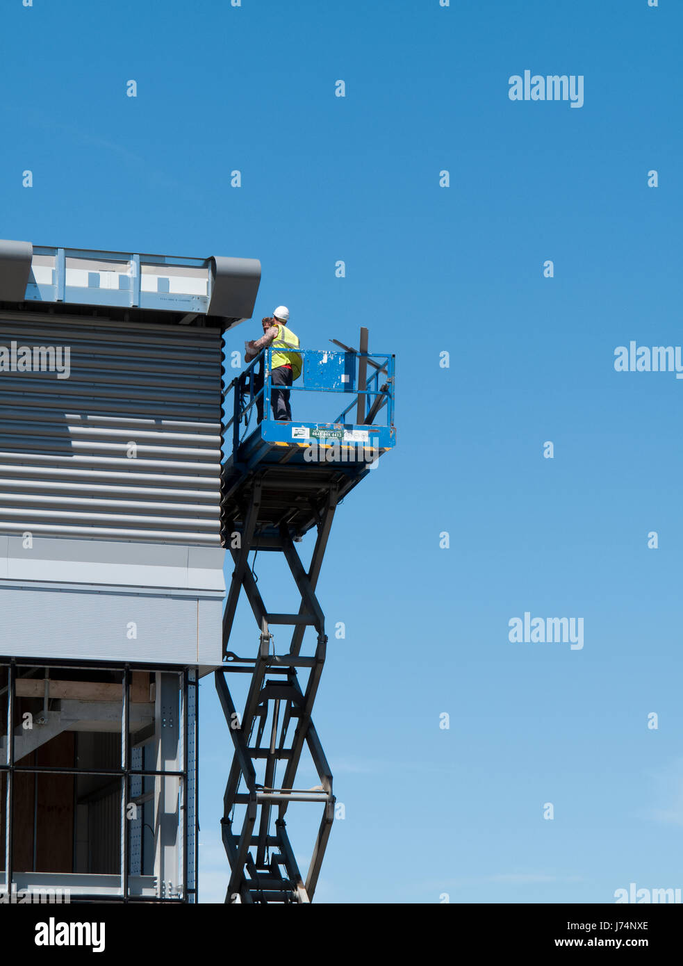 construction workers on mobile scissor lift installing cladding to new