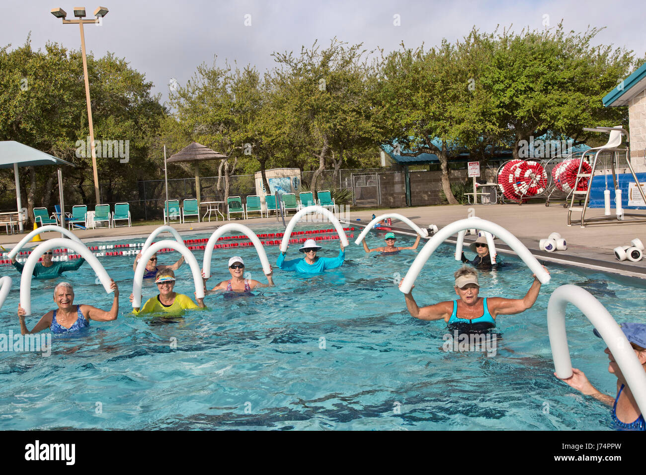 Group of  smiling happy senior women attending Water Aerobics class, using styrofoam  'water noodles', outdoor heated pool. Stock Photo