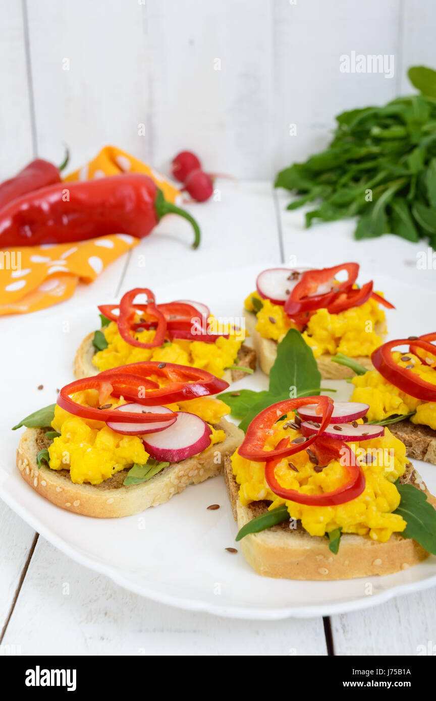 Sandwich with scrambled eggs, rucola, radish, paprika kapi and flax seeds on a plate on a light