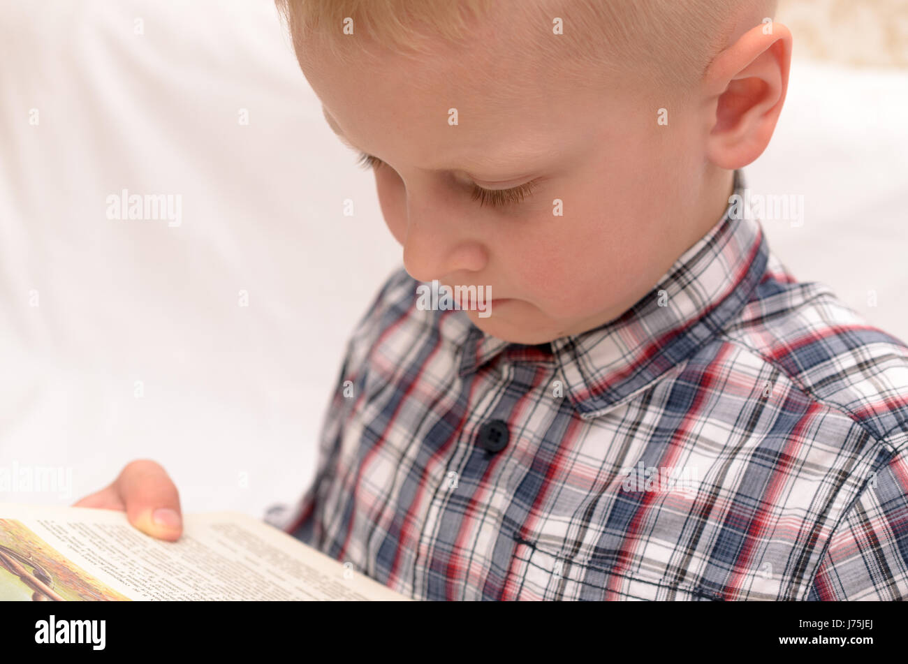 A fiveyearold boy reads a book on the bed and expresses emotions