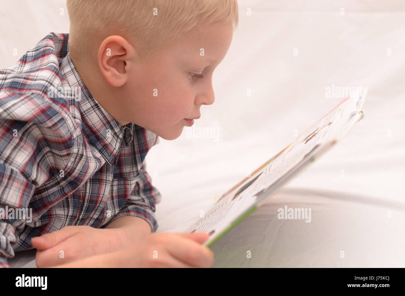 A fiveyearold boy reads a book on the bed and expresses emotions