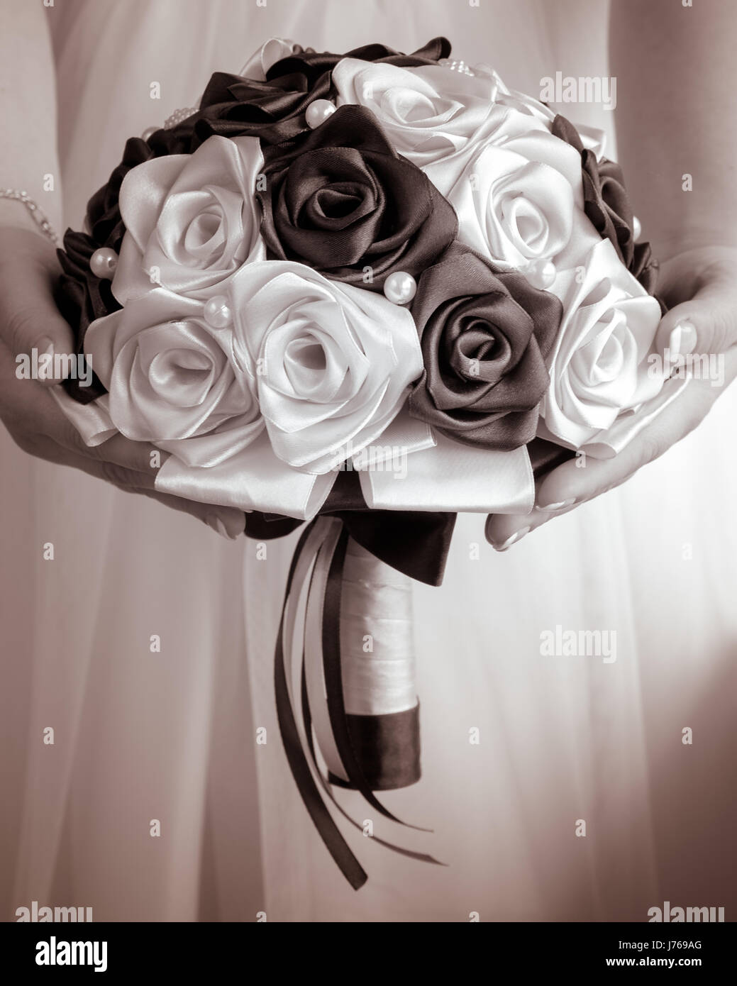 The bride's bouquet in hands on background of the wedding dress in monochrome tones Stock Photo