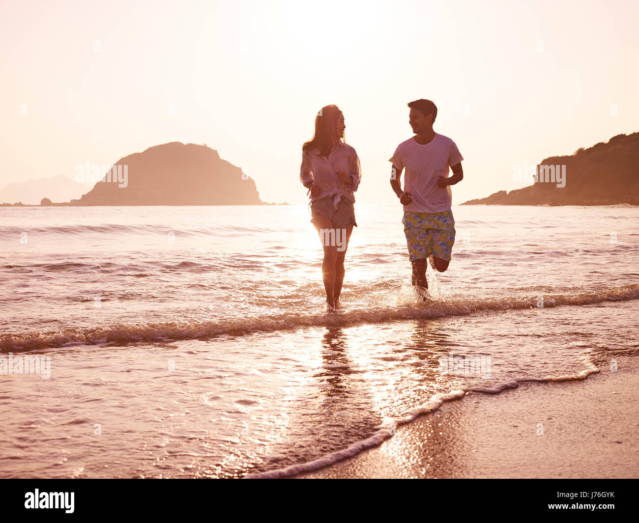 happy young asian couple running on beach in early morning. Stock Photo