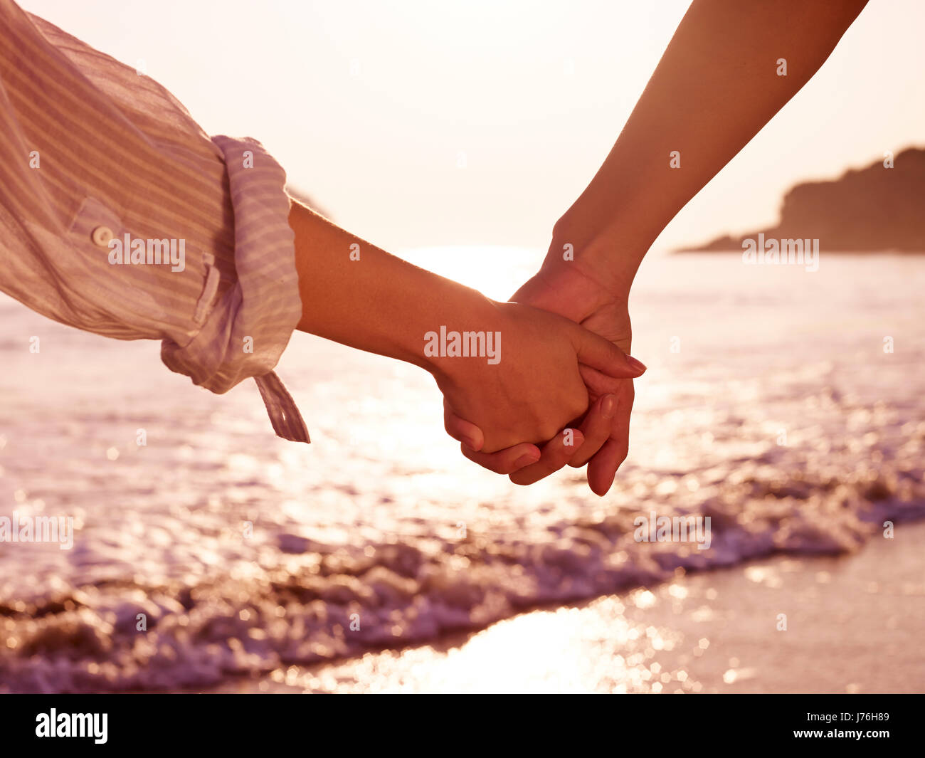 young couple lovers holding hands watching tide at beach. Stock Photo