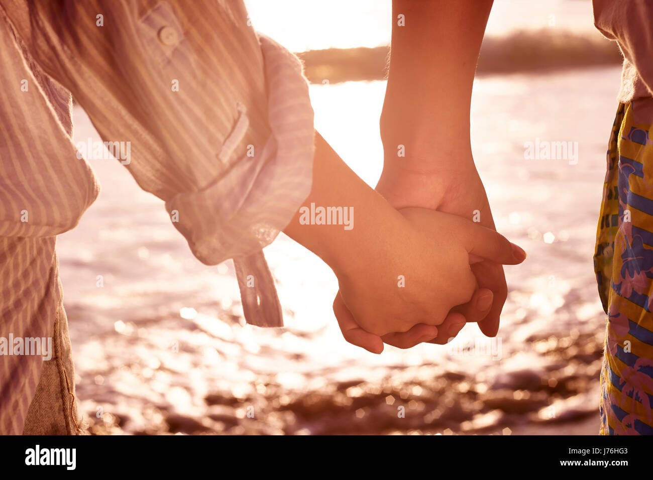 young couple lovers holding hands watching tide at beach. Stock Photo