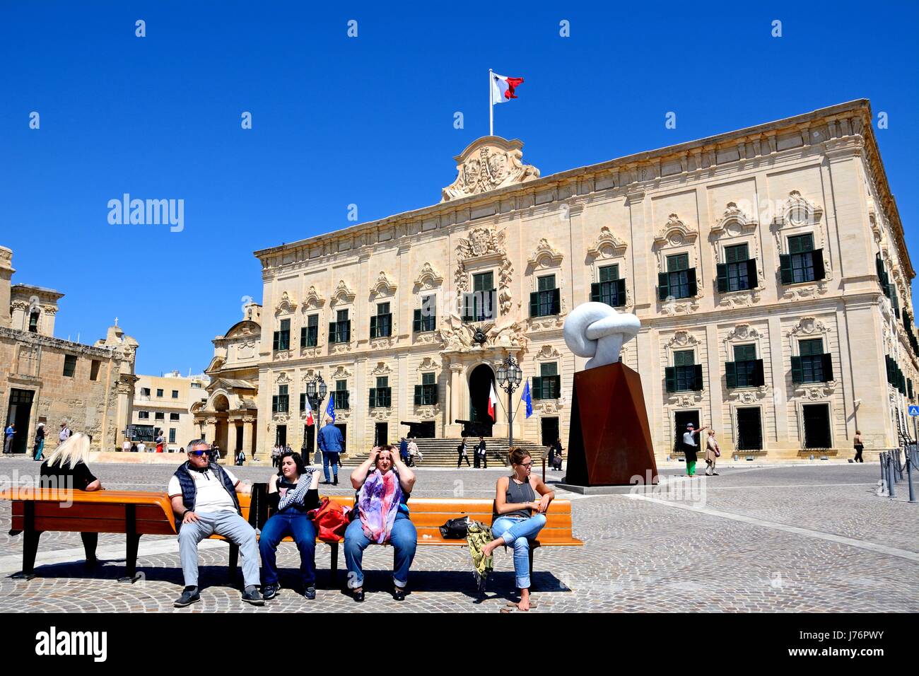 View of the Auberge de Castille in Castille Square with the Bianco Carrara marble sculpture and tourists sitting on a bench in the foreground, Vallett Stock Photo