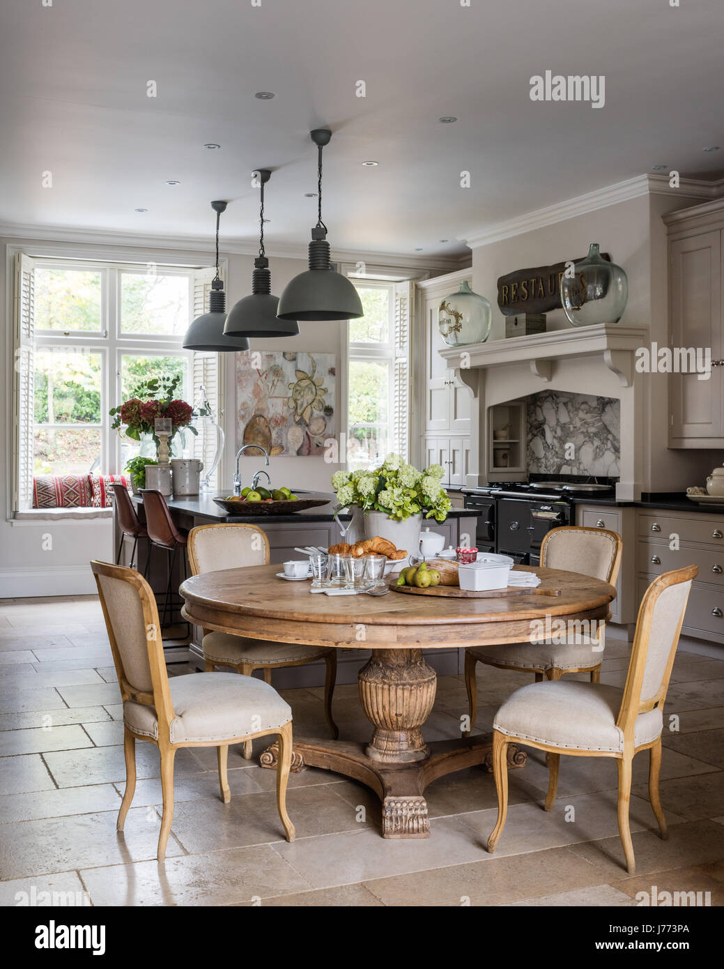 Spacious kitchen diner with limestone floor tiles and bespoke kitchen units by Thomas Ford & Sons. Circular table and chairs all by Bardoe & Appel. Stock Photo