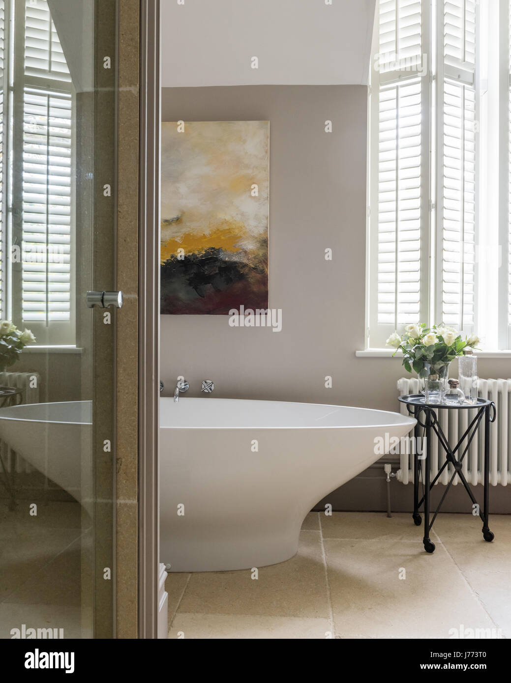 Napoli freestanding bath by Victoria & Albert in bathroom with painting by Susanne Winter and limestone floor tiles Stock Photo