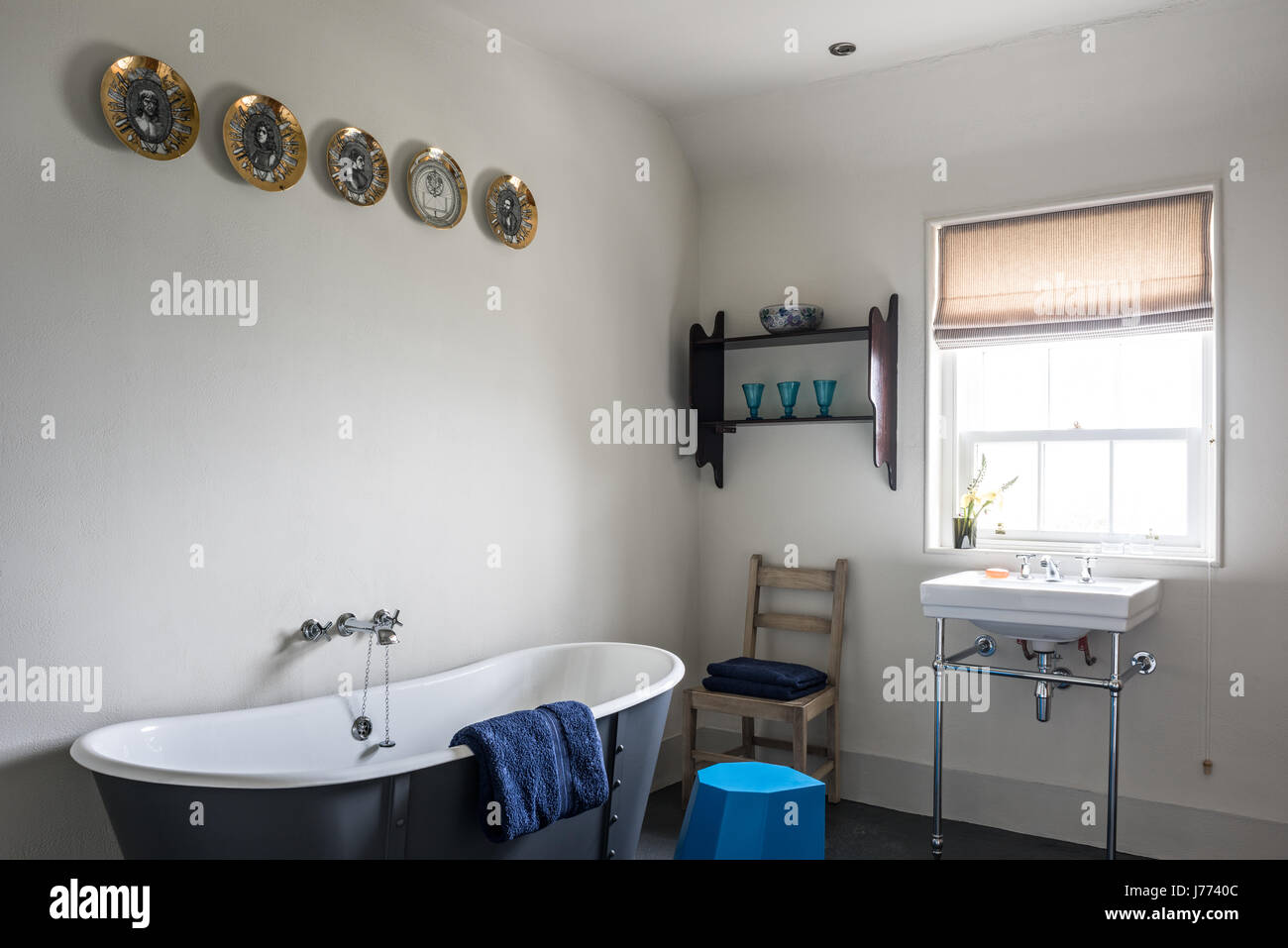 Decorative plates above grey freestanding bath in 17th century stone cottage bathroom, with stool by Martino Gamper Stock Photo