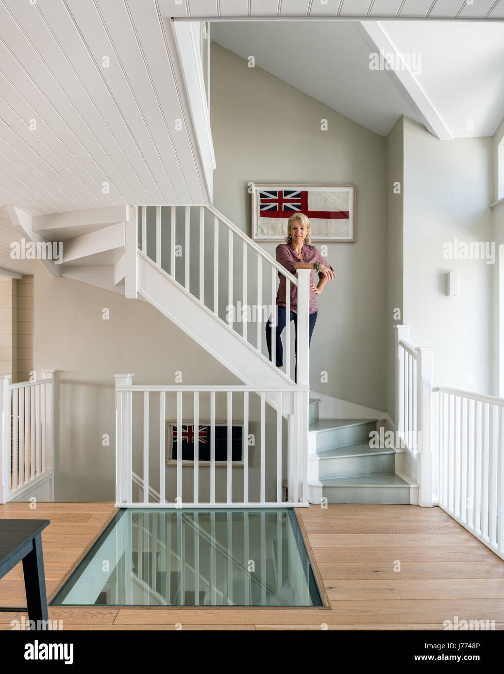 Glass floor on first storey landing with framed old british flags along the staircase. The walls are painted in Quill Grey by Sanderson. Stock Photo
