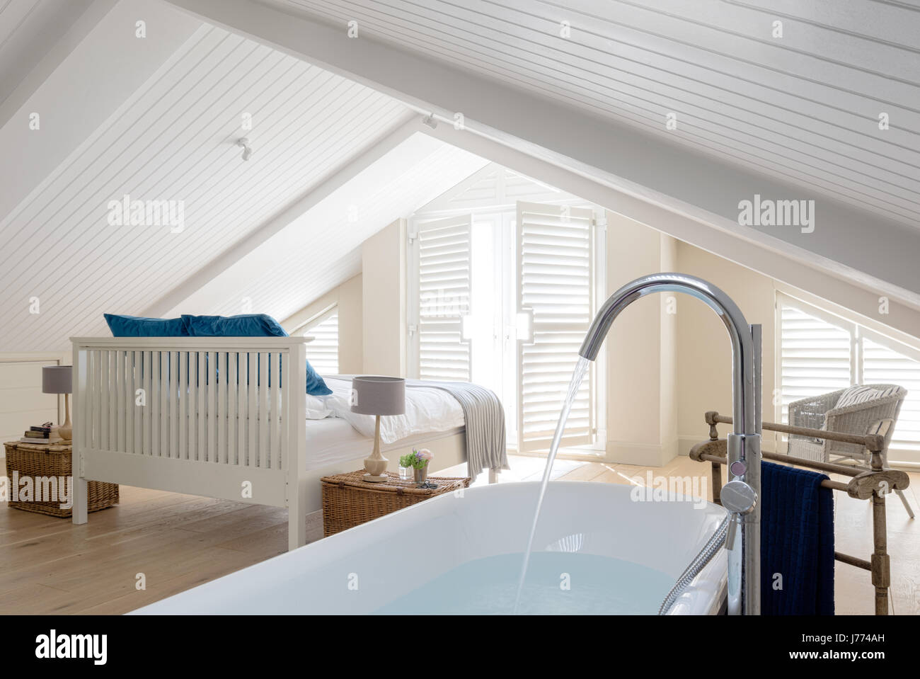 Free standing bath in top floor master bedroom with pitched ceiling and shutters. Hampers from Fortnum & Mason have been used as bedside tables Stock Photo