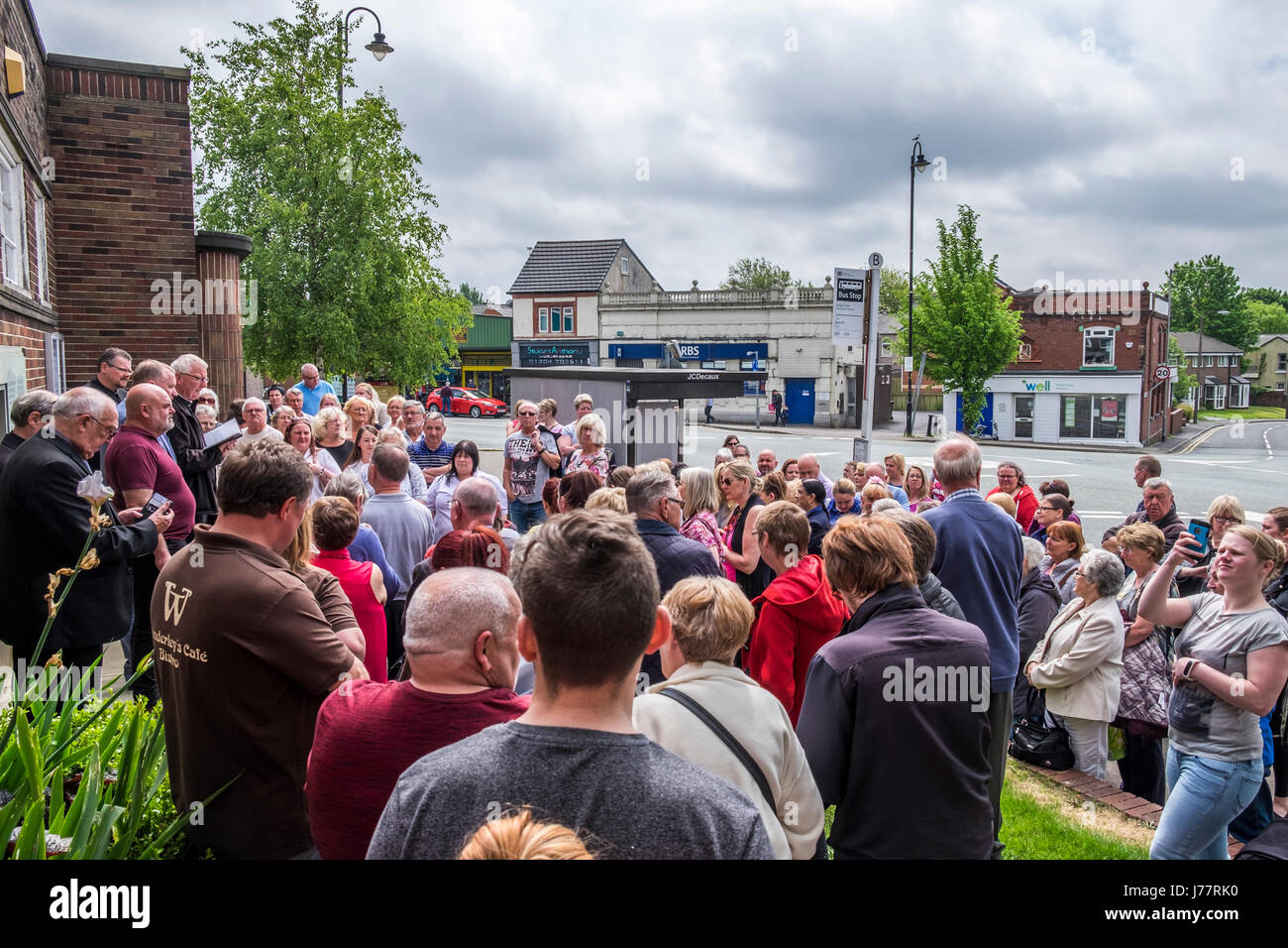 Little Lever, Bolton, England, 24th May 2017. Local priest leads members of the public in prayers for the victims and relatives of the Manchester bombing, local councillors, Sean Hornsby, Rees Gibbon, both Ukip members, Canon Ian Anthony. Members of the public, Local priest and UKIP councillors assemble to lead the general public in prayers for the family and victims of the recent Islamic State group bombing in the center of Manchester. Mike Hesp/ Alamy Live News. Stock Photo